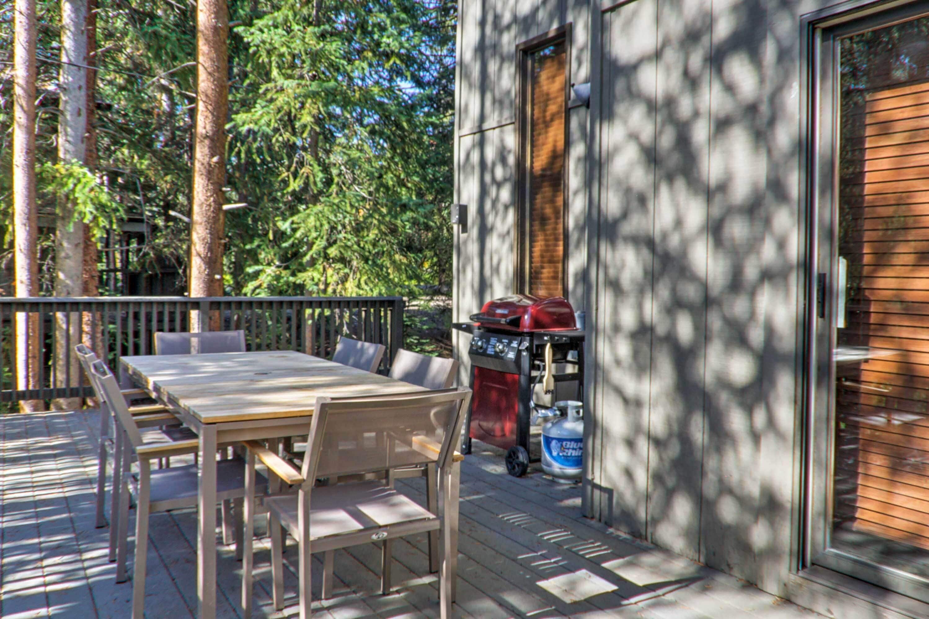 A deck with a wooden table and chairs, a barbecue grill, and a propane tank.