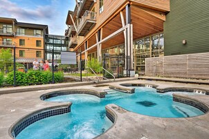Zona de piscina con varios jacuzzis, rodeada de edificios con balcones y ventanas amplias.