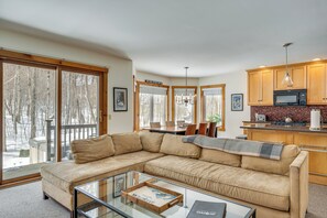 A modern living room with a beige sectional sofa, a glass coffee table, and a view of a deck with snow outside. - Ski-in Resort Family Condo w/ Deck at Jay Peak! (North Troy)