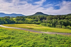 A golf course with a road running through it, surrounded by lush greenery and hills in the background.