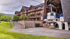 A multi-story lodge with a stone facade, wooden balconies, and a ski lift visible. - Ski-in Resort Family Condo w/ Deck at Jay Peak! (North Troy)