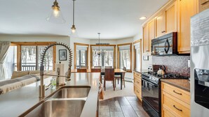 A modern kitchen with a central island, stainless steel appliances, wooden cabinets, and large windows. - Ski-in Resort Family Condo w/ Deck at Jay Peak! (North Troy)