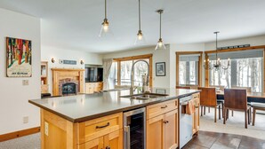 A modern kitchen with a central island, pendant lights, a fireplace, and large windows. - Ski-in Resort Family Condo w/ Deck at Jay Peak! (North Troy)