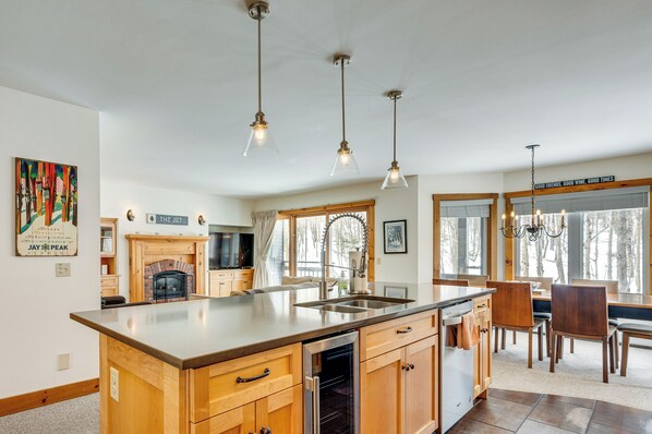 A modern kitchen with a central island, wooden cabinetry, and pendant lighting. - Ski-in Resort Family Condo w/ Deck at Jay Peak! (North Troy)