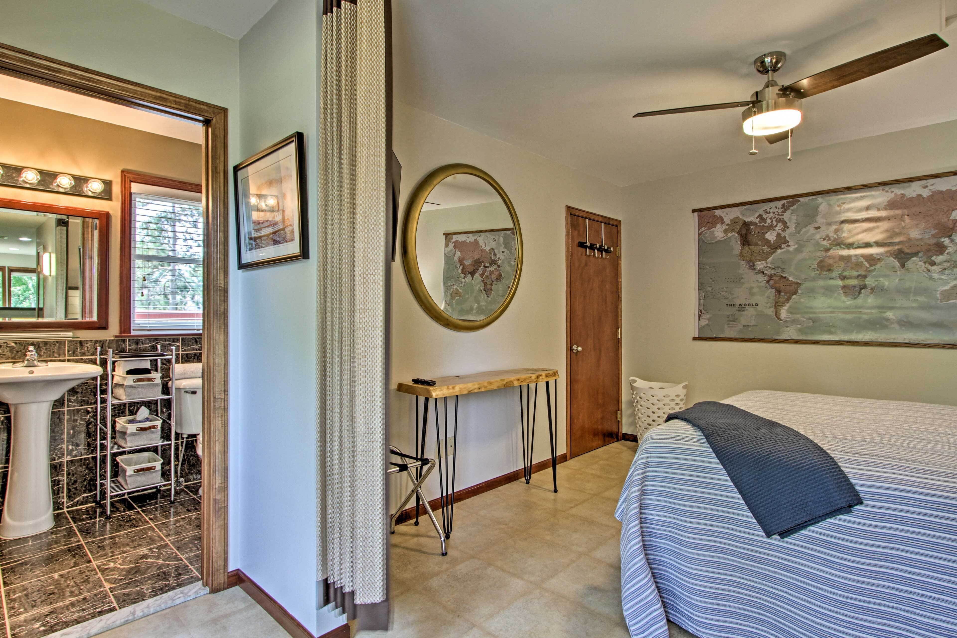 A bedroom with a bed, a desk, a chair, a mirror, a sink, and a map on the wall.