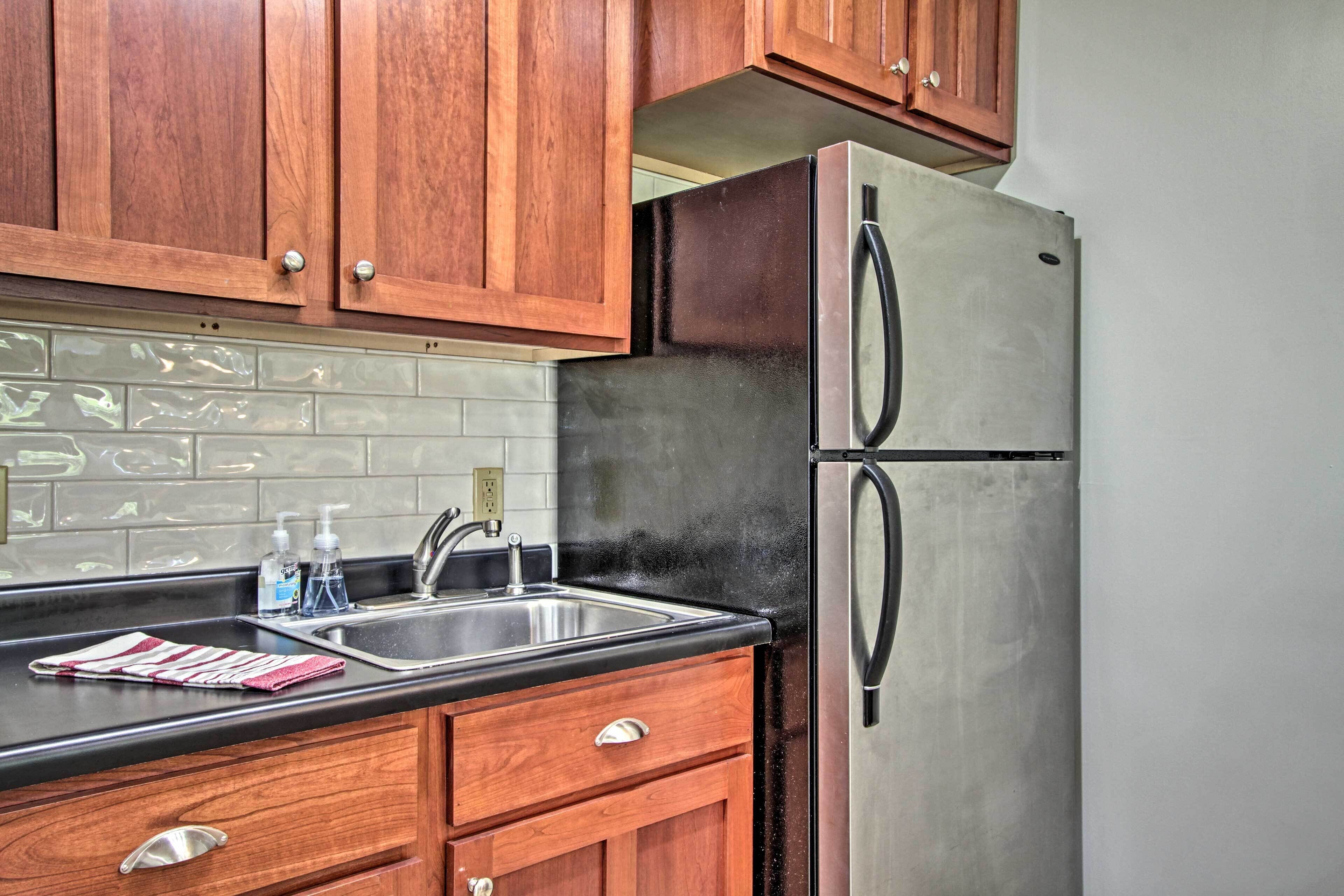 A kitchen with wooden cabinets, a stainless steel refrigerator, a black countertop, and a tiled backsplash.