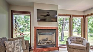 A living room with a fireplace, a television mounted above it, and a large window offering a view of the outdoors. - Pet-friendly Wabasha Studio: Boat, Ski & Explore! (Wabasha)