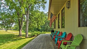 A wooden deck with Adirondack chairs lined up against a building with a flag. - Pet-friendly Wabasha Studio: Boat, Ski & Explore! (Wabasha)