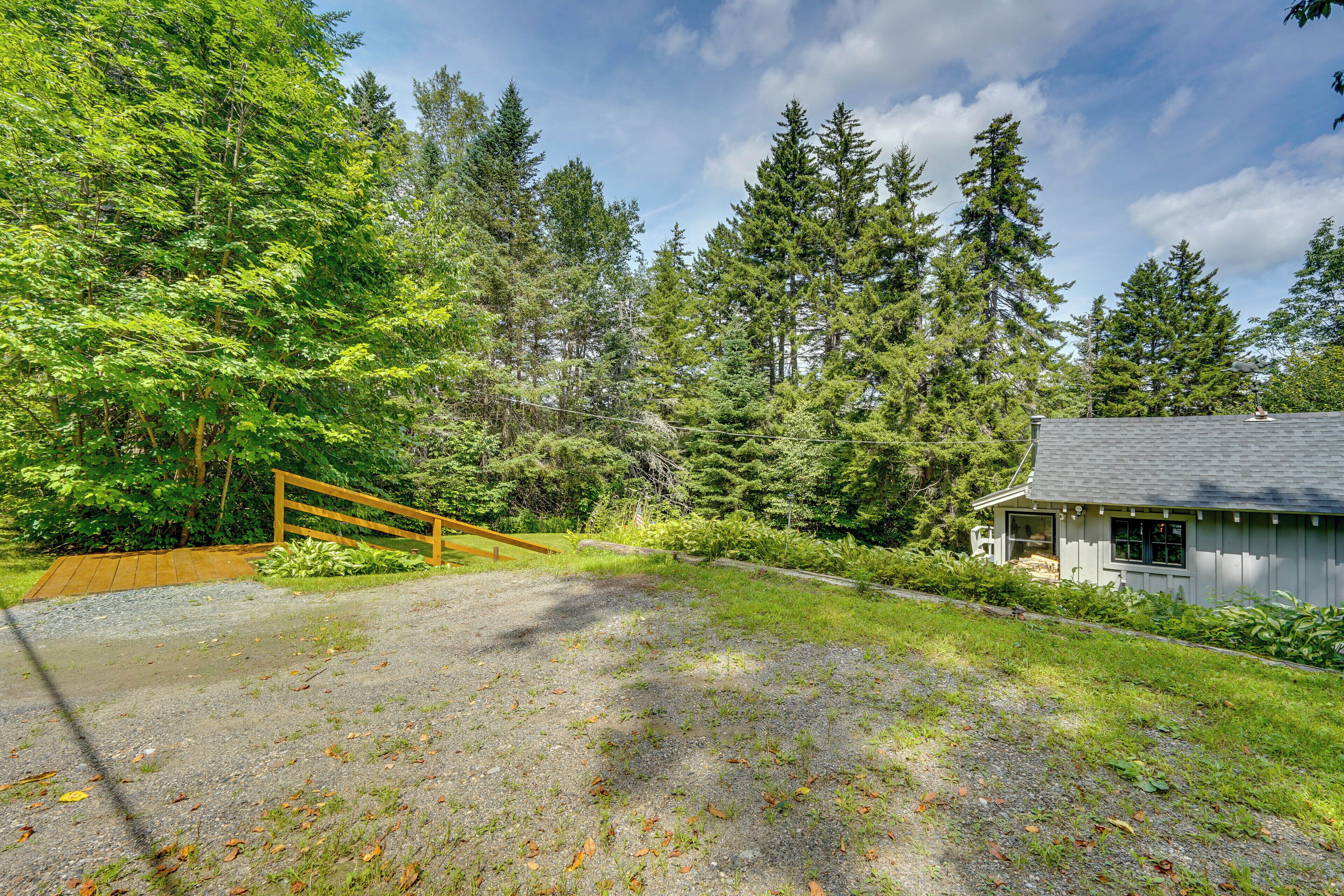 A house with a gravel driveway, a wooden fence, and a forested area.