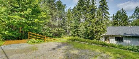 A house with a gravel driveway, a wooden fence, and a forested area.