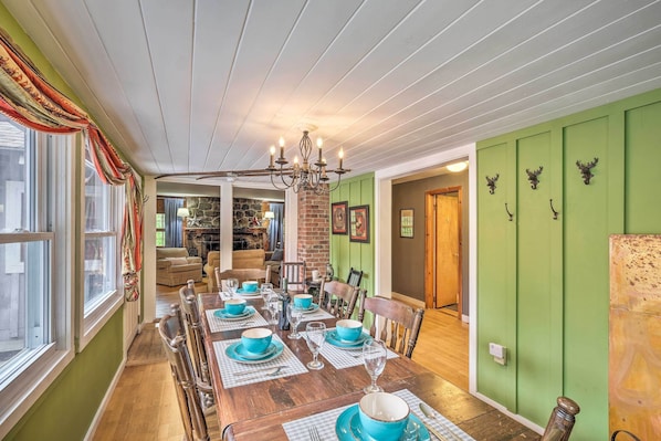 Uma sala de jantar com uma mesa de madeira posta para seis pessoas, paredes verdes e um candelabro.