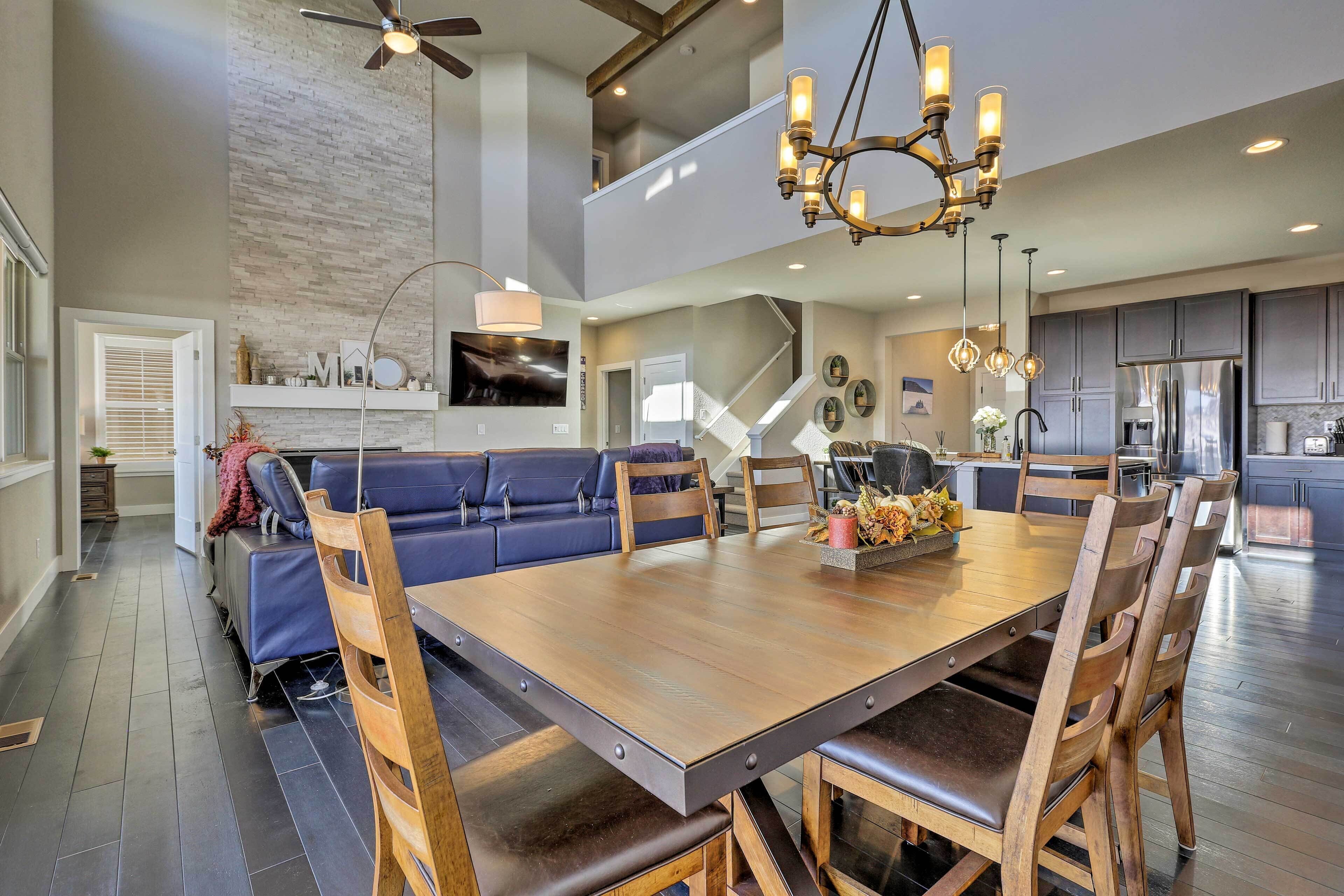 A spacious dining area with a large wooden table and chairs, a ceiling fan, and a modern kitchen in the background.