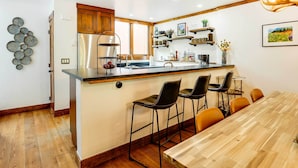 A modern kitchen with a central island, bar stools, and a dining table.