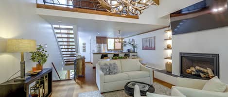 Amplia sala de estar con chimenea, una escalera y una cocina al fondo.