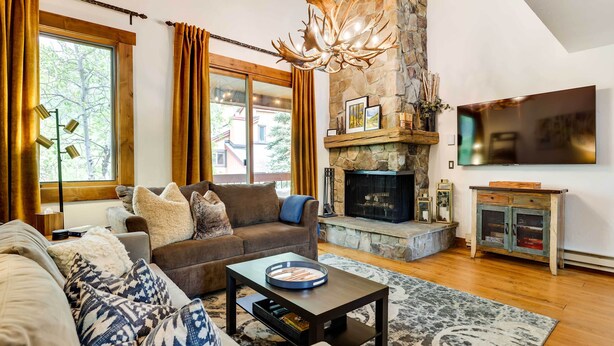A living room with a stone fireplace, a flat-screen TV, and a large window with curtains.