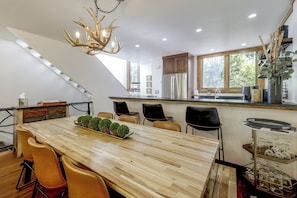 Une cuisine moderne dotée d’un îlot central, d’un coin repas avec une longue table en bois et d’un lustre orné de luminaires en forme de bois de cerf.