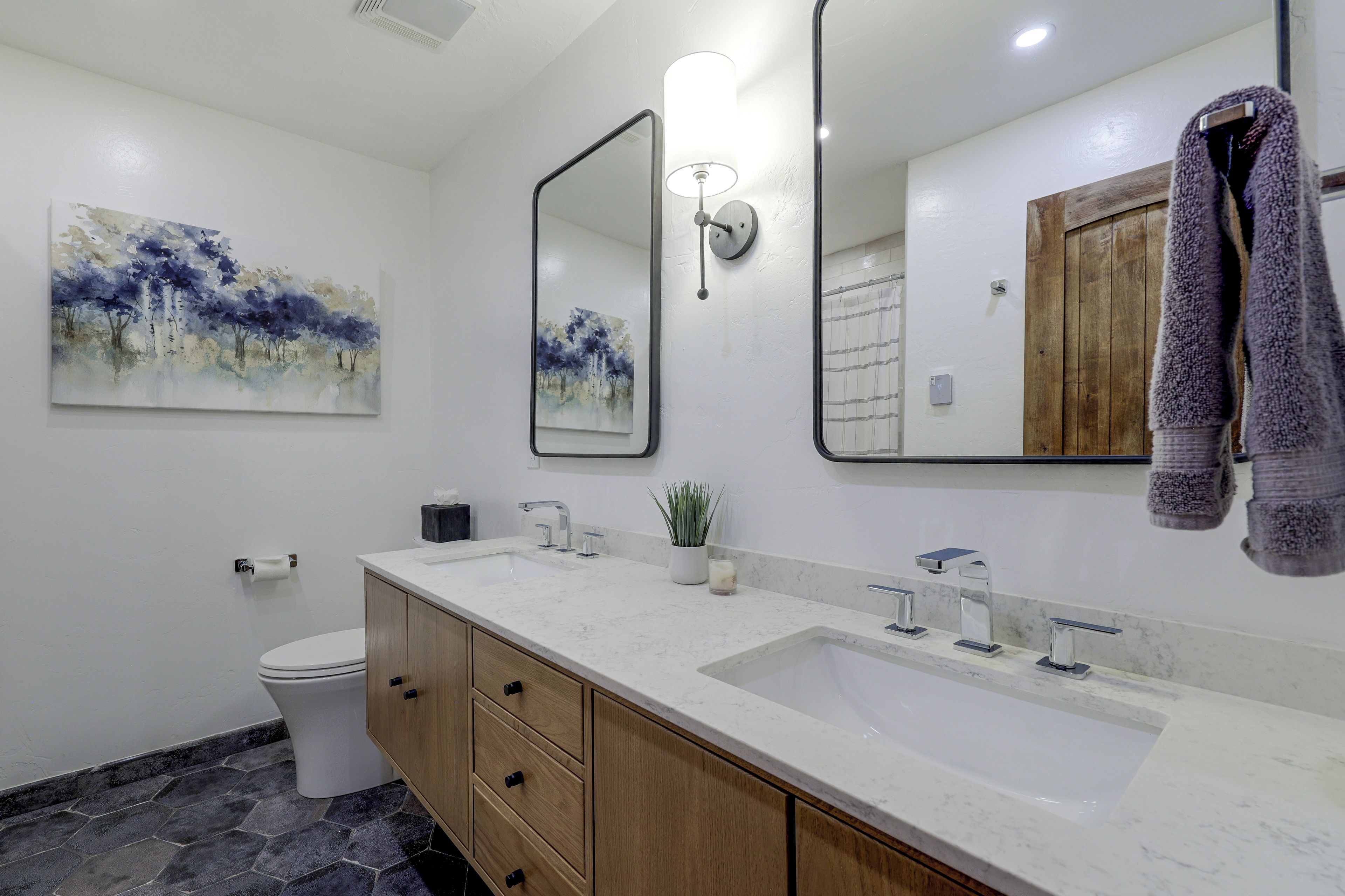 Une salle de bain avec un lavabo blanc, des meubles en bois, des toilettes et un tableau accroché au mur.