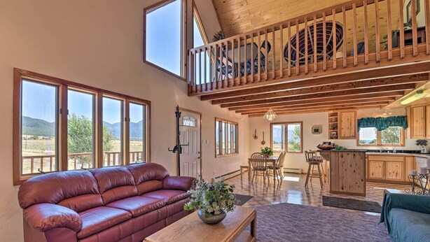A spacious living area with a leather sofa, wooden coffee table, and a view of mountains through large windows. - Questa Home w/ Views - 13 Mi to Red River Skiing! (Questa)