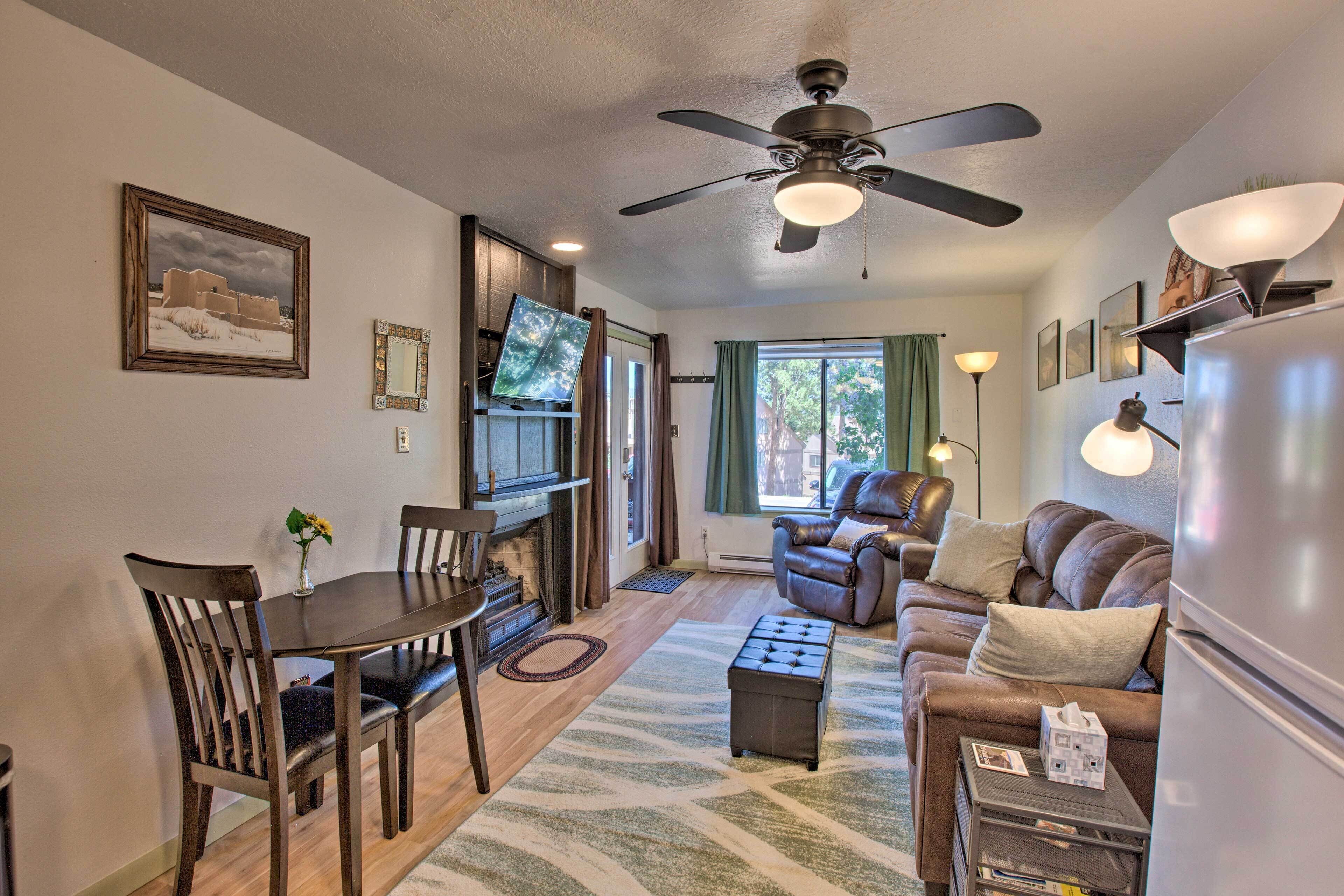 A living room with a fireplace, a ceiling fan, a television, a sofa, and a dining area with chairs and a table.