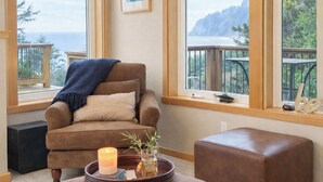Una habitación acogedora con un sillón marrón, una mesita con una vela y vistas al océano a través de amplios ventanales.