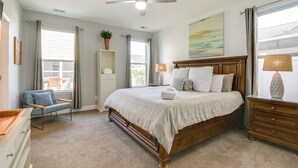 Un dormitorio con cama, una silla, cómoda, ventilador de techo y ventana con cortinas.