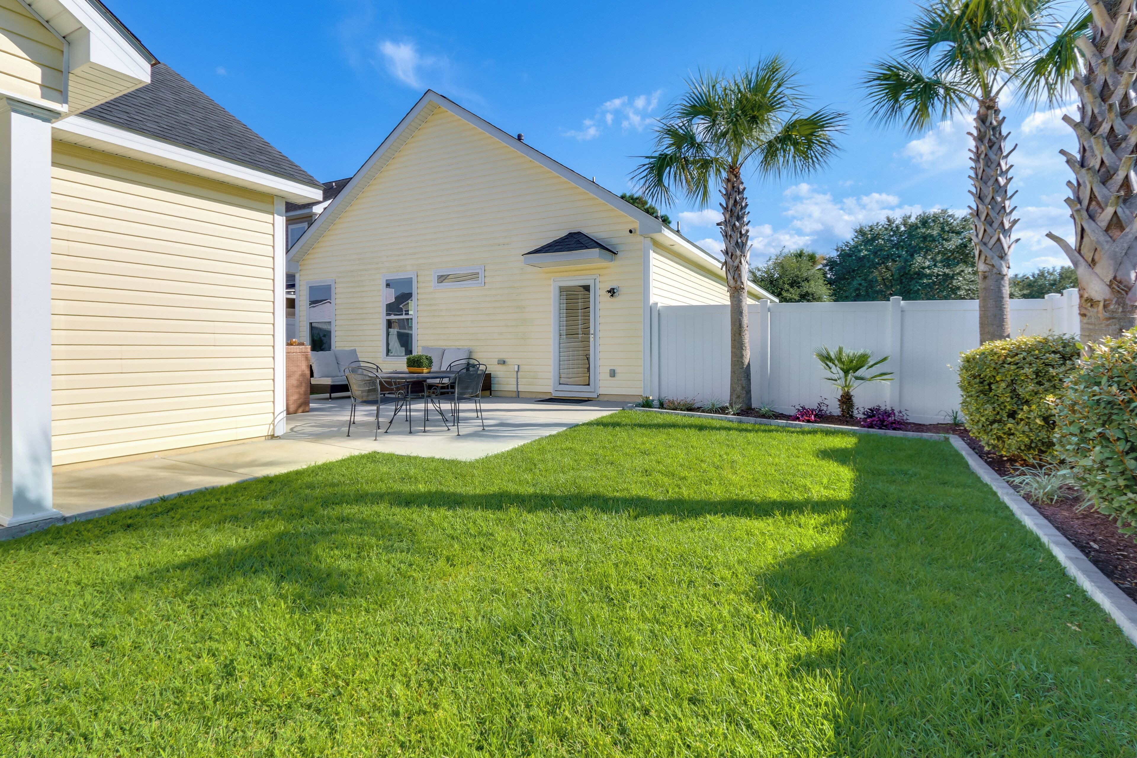 A residential backyard with a lawn, a patio table, chairs, and a white fence.