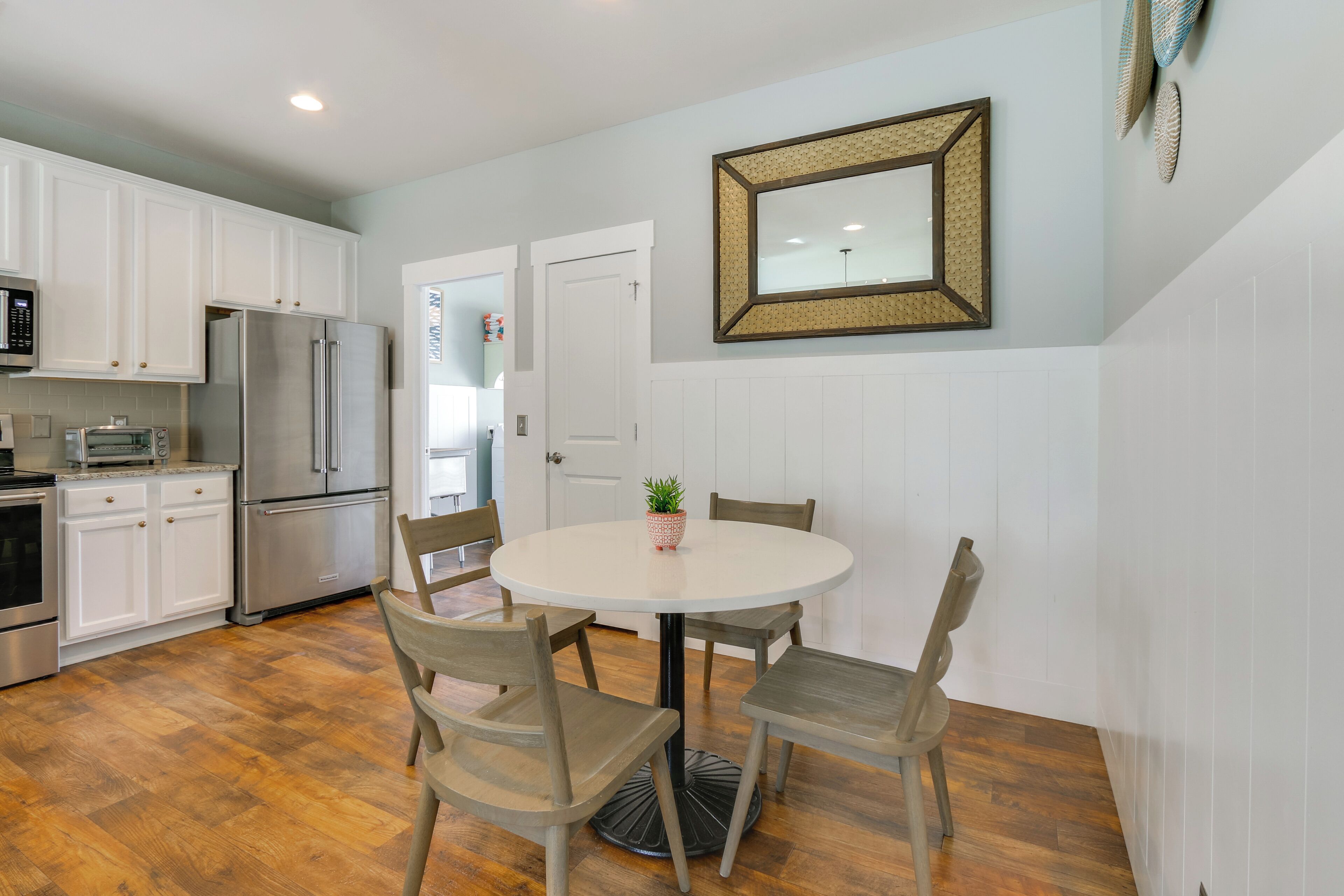 A kitchen with white cabinets, a stainless steel refrigerator, a microwave, and a dining table with four chairs.