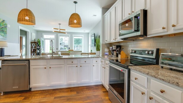 Una cocina moderna con muebles blancos, electrodomésticos de acero inoxidable y piso de madera.