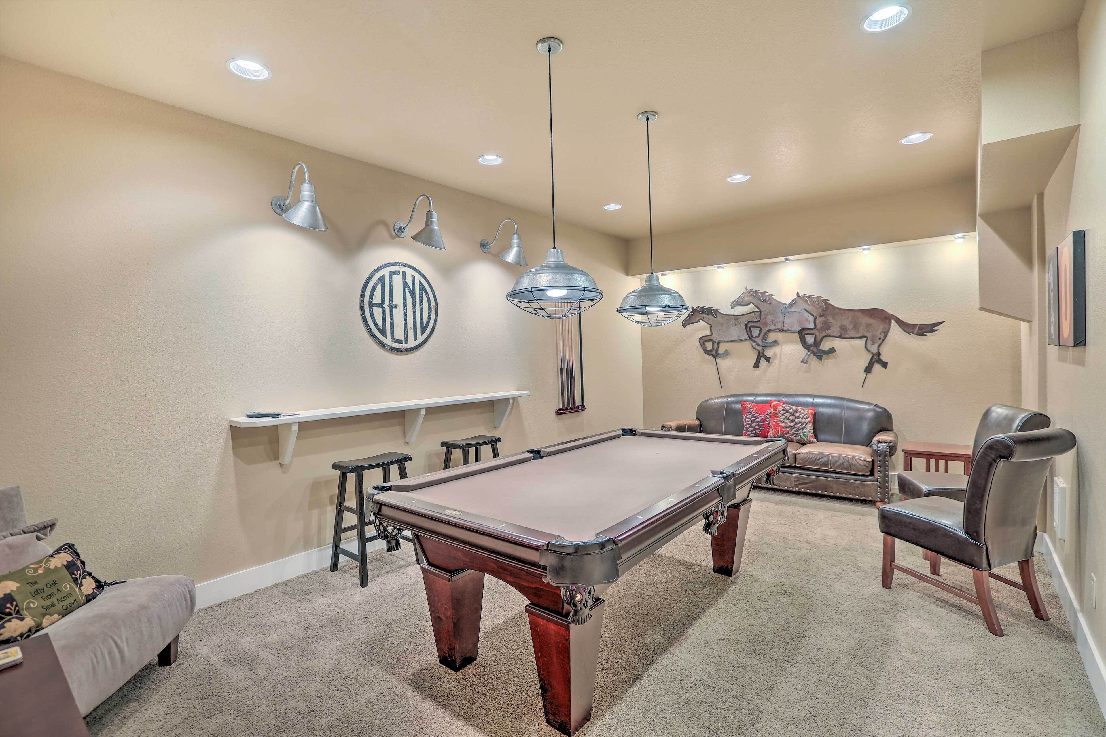 A pool table in a room with a beige carpet, a sofa, a chair, and wall-mounted lights.