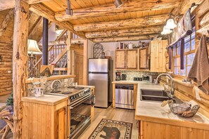 A rustic cabin-style kitchen with wooden beams, a stainless steel refrigerator, a dishwasher, and a stove.