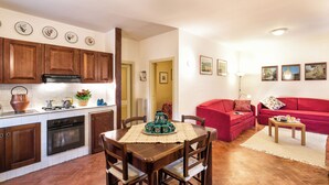 A compact kitchen with wooden cabinets and a dining area with a table and chairs. There is a red sofa in the living area. - Apartment with terrace (Rasiglia)