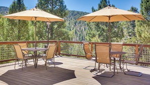 Eine Holzterrasse mit Gartenmöbeln und Sonnenschirmen, mit Blick auf eine bewaldete Landschaft.