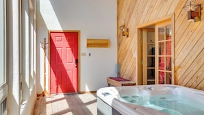 Ein Zimmer mit Holzwänden, einer roten Tür, einer Holzbank und einer Whirlpool-Badewanne.
