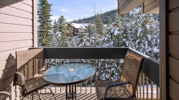 A balcony with a table and chairs, overlooking a snowy mountain landscape.