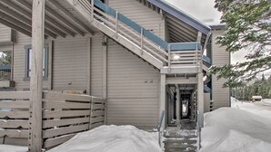 A building with a wooden exterior, a staircase leading to a balcony, and a snow-covered ground.