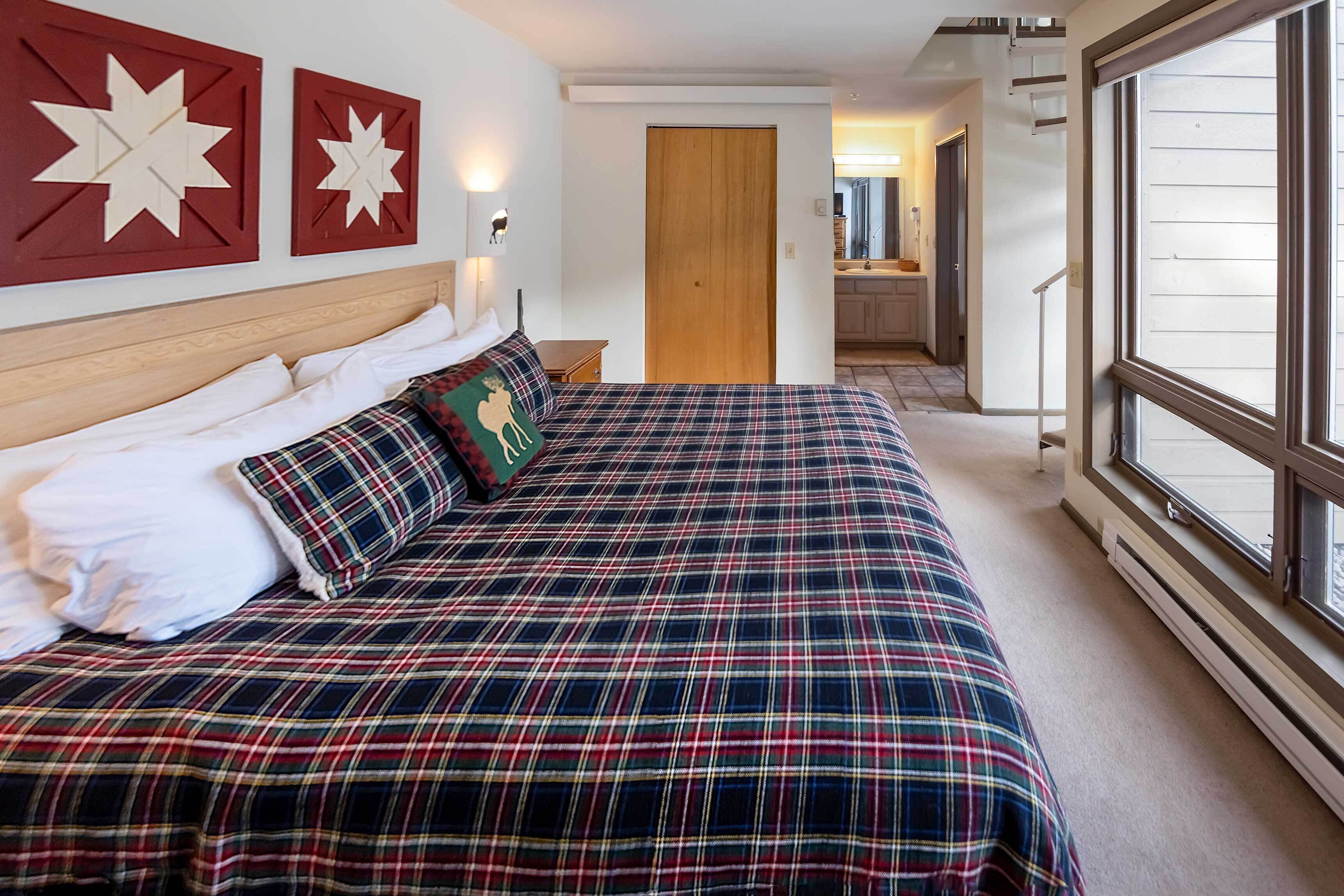 A bedroom with a plaid bedspread, a wooden headboard, and two wall-mounted star decorations.