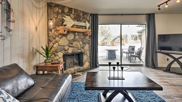 A modern living room with a stone wall, a fireplace, a leather sofa, a coffee table, and a view through large glass doors. - Pagosa Springs Condo w/ Patio, 4 Mi to Hot Springs (Pagosa Springs)