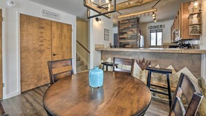 A dining area with a round wooden table, chairs, a blue vase, and a chandelier. There are wooden cabinets above the counter and a sign indicating a dining area. - Pagosa Springs Condo w/ Patio, 4 Mi to Hot Springs (Pagosa Springs)
