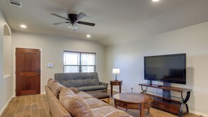 Una sala de estar con un sofá modular, un televisor sobre un mueble de madera, un ventilador de techo y una ventana con persianas.