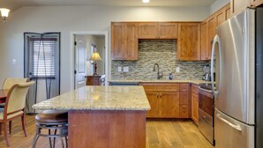 Una cocina con armarios de madera, encimera de granito, refrigerador de acero inoxidable y horno empotrado.
