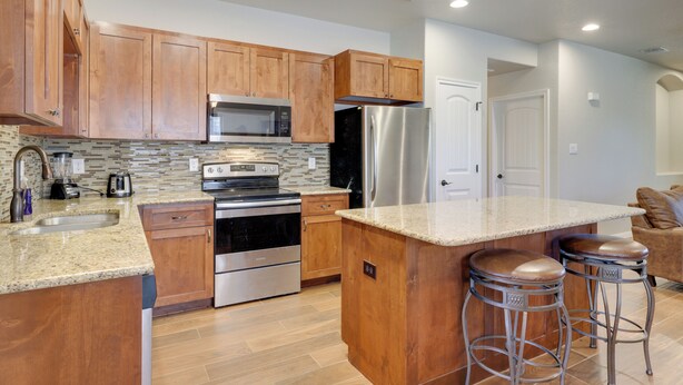 Una cocina moderna con armarios de madera, electrodomésticos de acero inoxidable, encimera de granito y una zona con taburetes de bar.