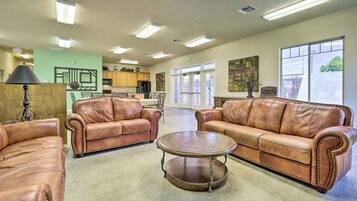 A spacious living area with leather sofas, a coffee table, and a kitchen in the background.