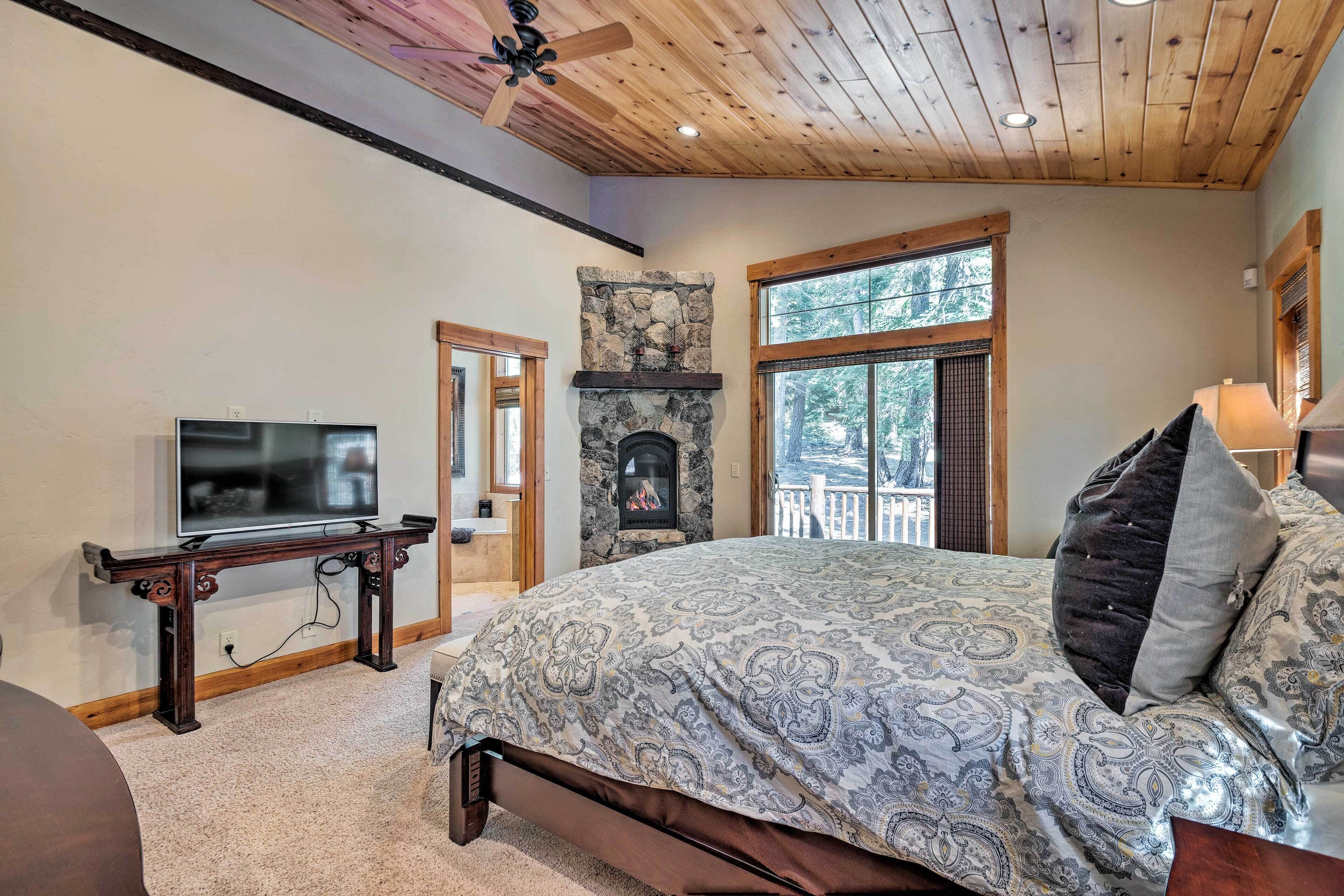 Une chambre avec une cheminée en pierre, un téléviseur posé sur une console en bois et un grand lit avec une literie à motifs.