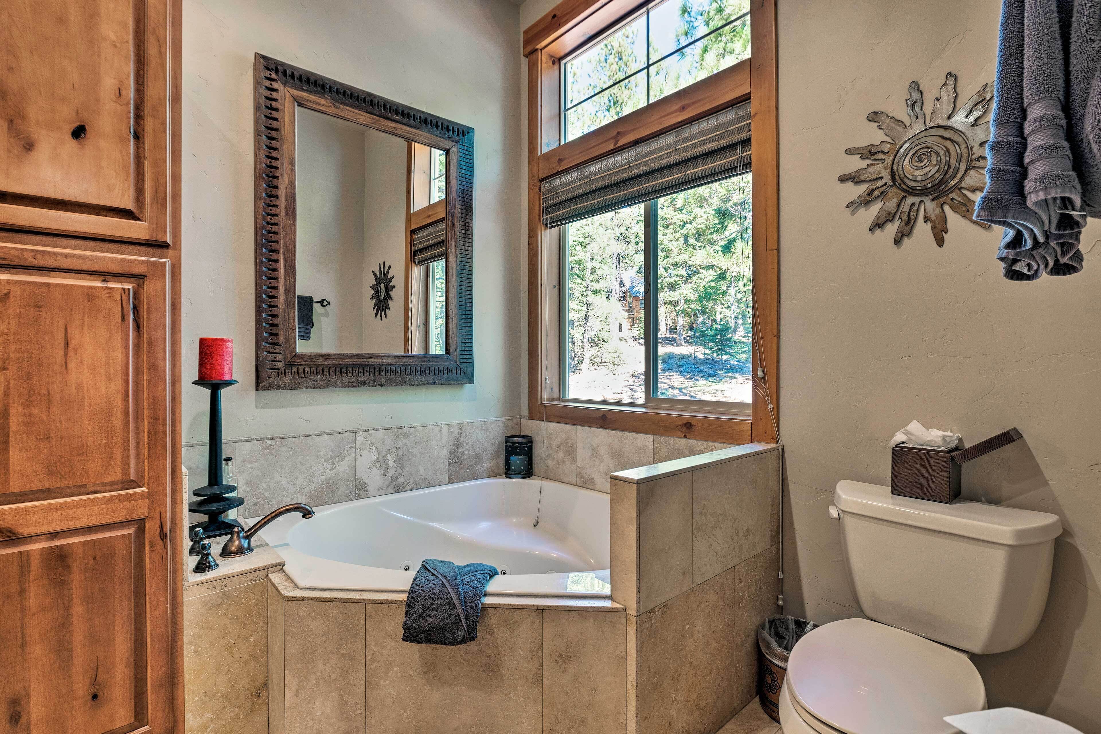 A bathroom with a bathtub, a toilet, a window, and wooden cabinets.