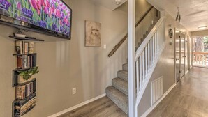 A home interior with a staircase, a mounted television, and a bookshelf with books and a plant. - Forested Ruidoso Condo w/ Deck & Fireplace! (Ruidoso)