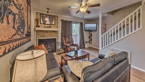 A living room with a fireplace, leather sofa, and a ceiling fan. - Forested Ruidoso Condo w/ Deck & Fireplace! (Ruidoso)