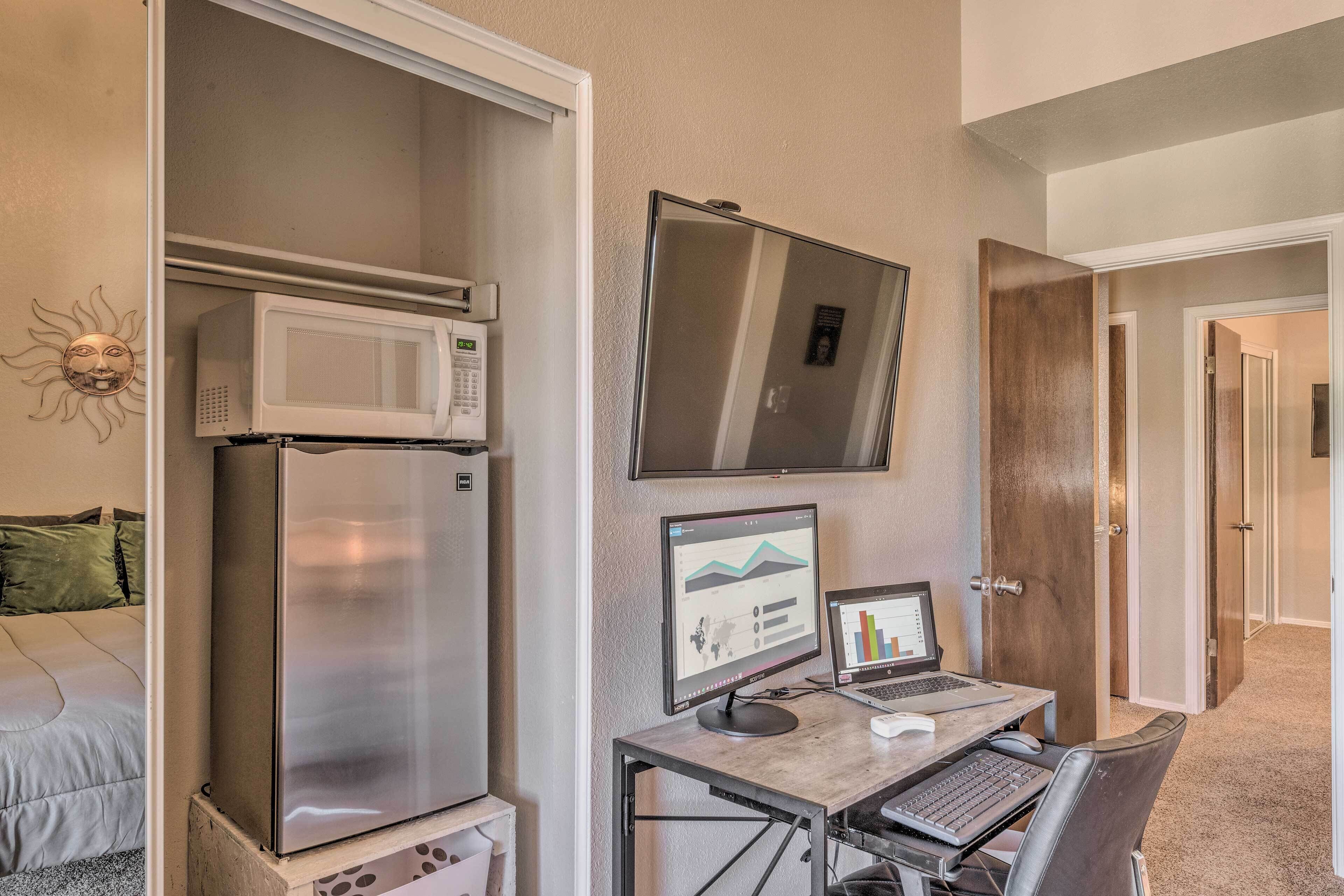 Una habitación de hotel compacta con kitchenette, un escritorio con ordenador y un espejo grande.