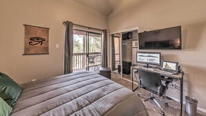 A bedroom with a bed, a desk with computers, a TV, and a window with curtains. - Forested Ruidoso Condo w/ Deck & Fireplace! (Ruidoso)