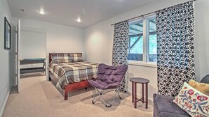 Um quarto com cama, uma poltrona roxa, uma mesinha, um sofá e cortinas estampadas.