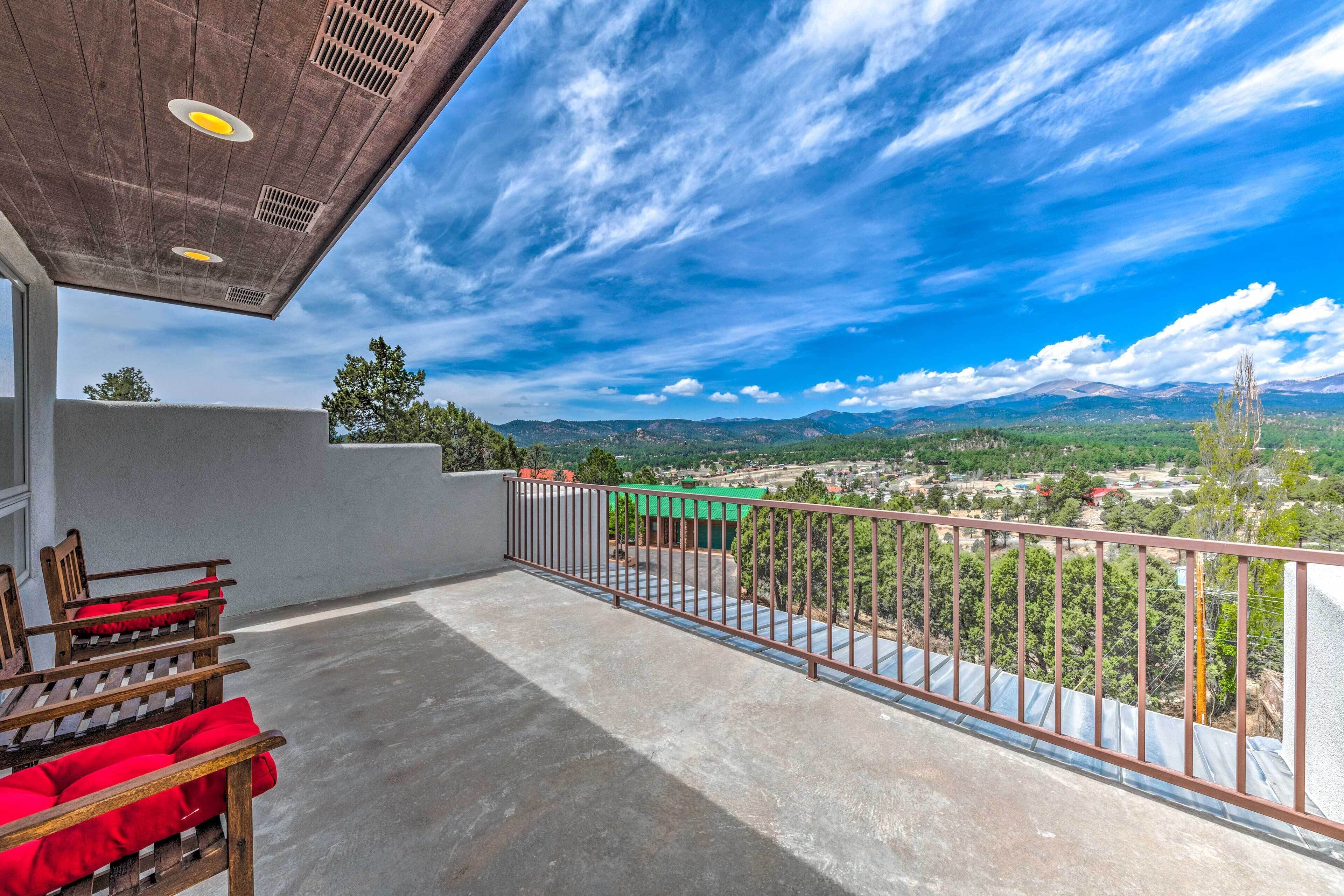 A balcony with a metal railing, a concrete floor, and a view of a town and mountains in the distance.